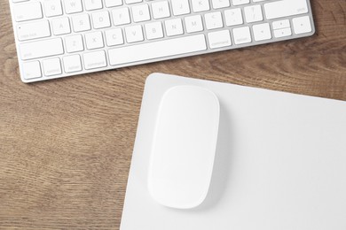 Photo of Computer mouse with mousepad and keyboard on wooden table, flat lay