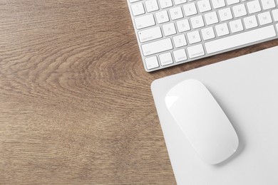 Photo of Computer mouse with mousepad and keyboard on wooden table, flat lay. Space for text