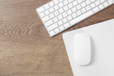 Photo of Computer mouse with mousepad and keyboard on wooden table, flat lay. Space for text