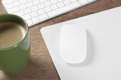 Photo of Computer mouse with mousepad, keyboard and cup of coffee on wooden table