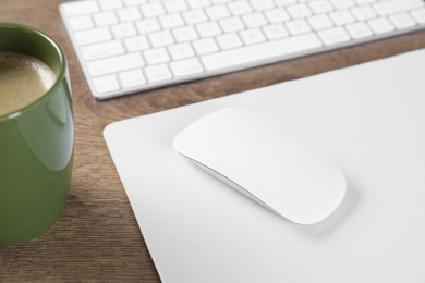 Photo of Computer mouse with mousepad, keyboard and cup of coffee on wooden table