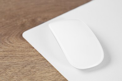 Photo of Computer mouse with mousepad on wooden table, closeup