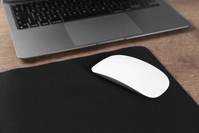 Photo of Computer mouse with mousepad and laptop on wooden table