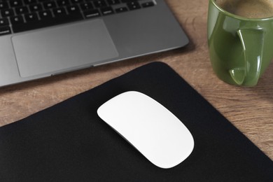 Photo of Computer mouse with mousepad, cup of coffee and laptop on wooden table