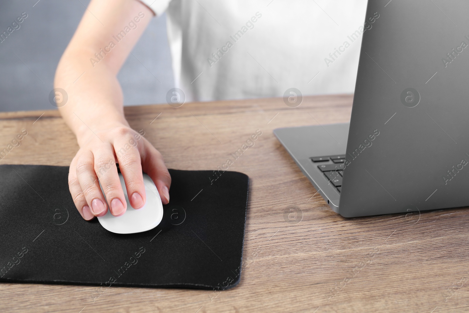 Photo of Woman using computer mouse while working with laptop at wooden table, closeup