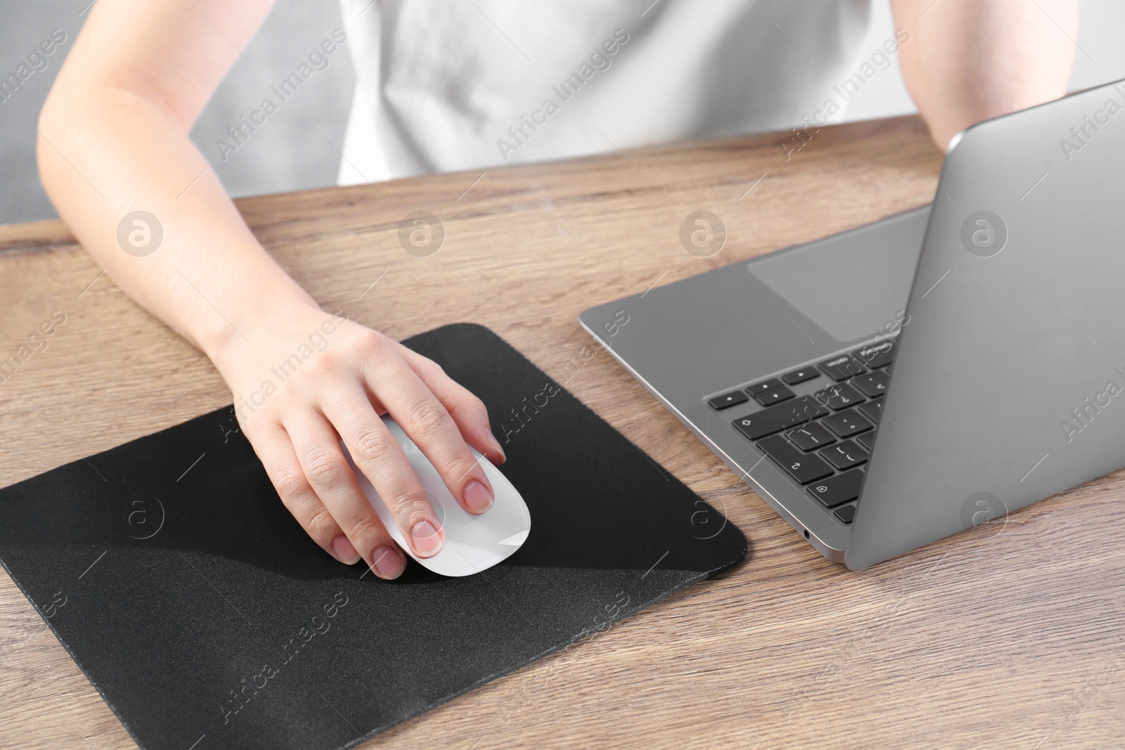 Photo of Woman using computer mouse while working with laptop at wooden table, closeup