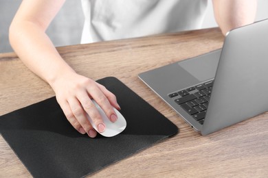 Photo of Woman using computer mouse while working with laptop at wooden table, closeup