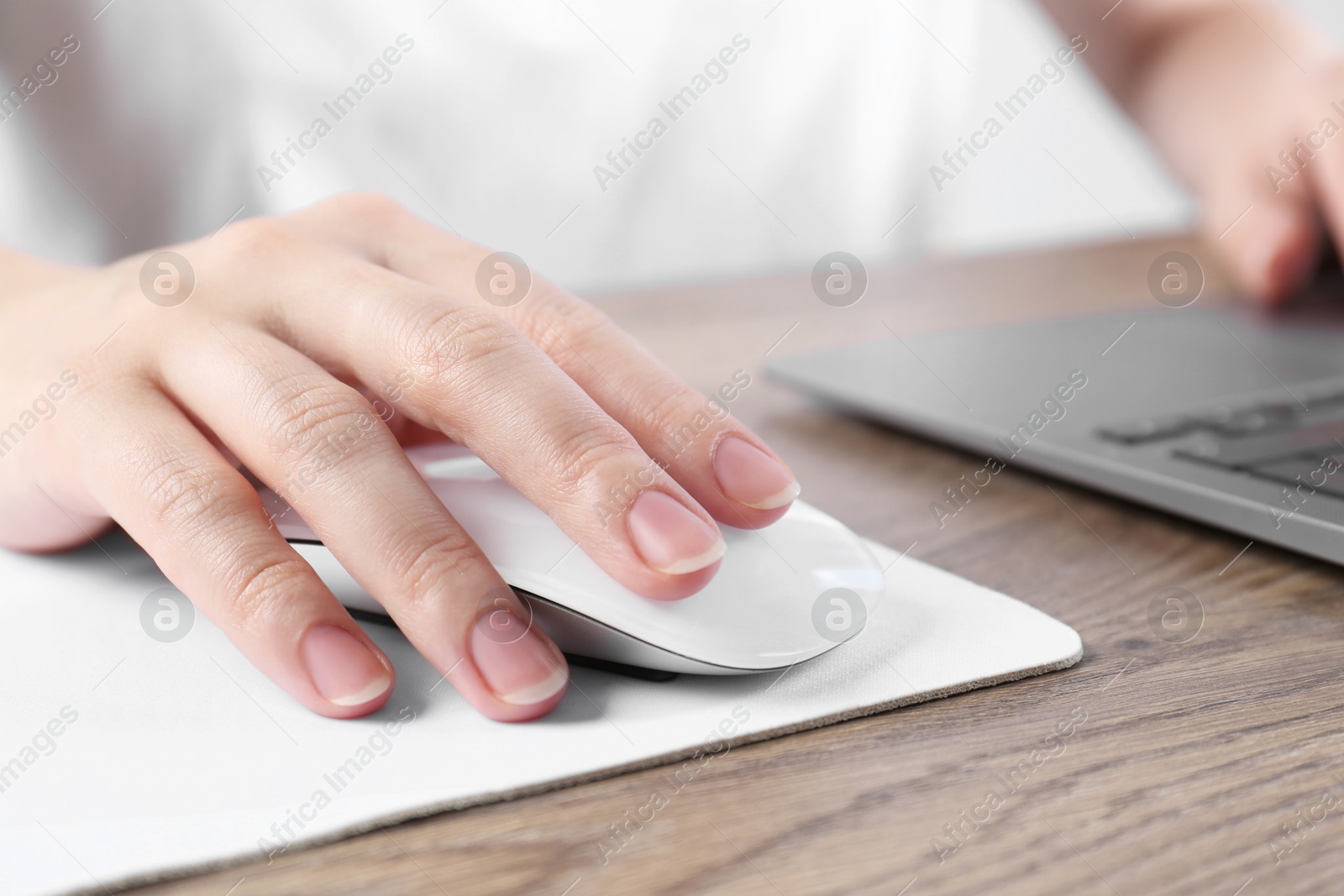 Photo of Woman using computer mouse while working with laptop at wooden table, closeup