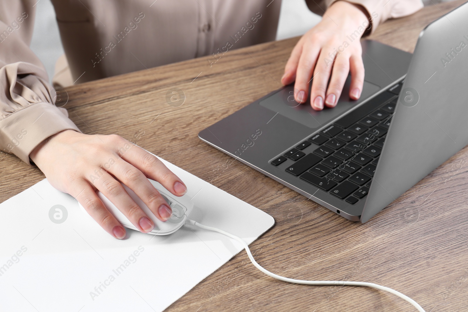 Photo of Woman using computer mouse while working with laptop at wooden table, closeup