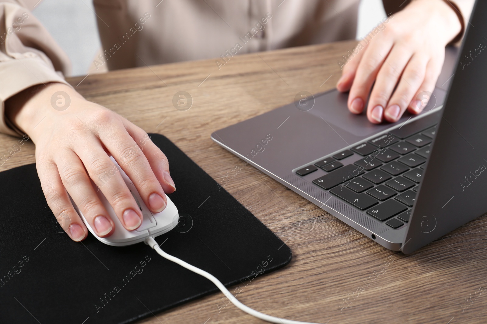 Photo of Woman using computer mouse while working with laptop at wooden table, closeup