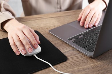 Photo of Woman using computer mouse while working with laptop at wooden table, closeup