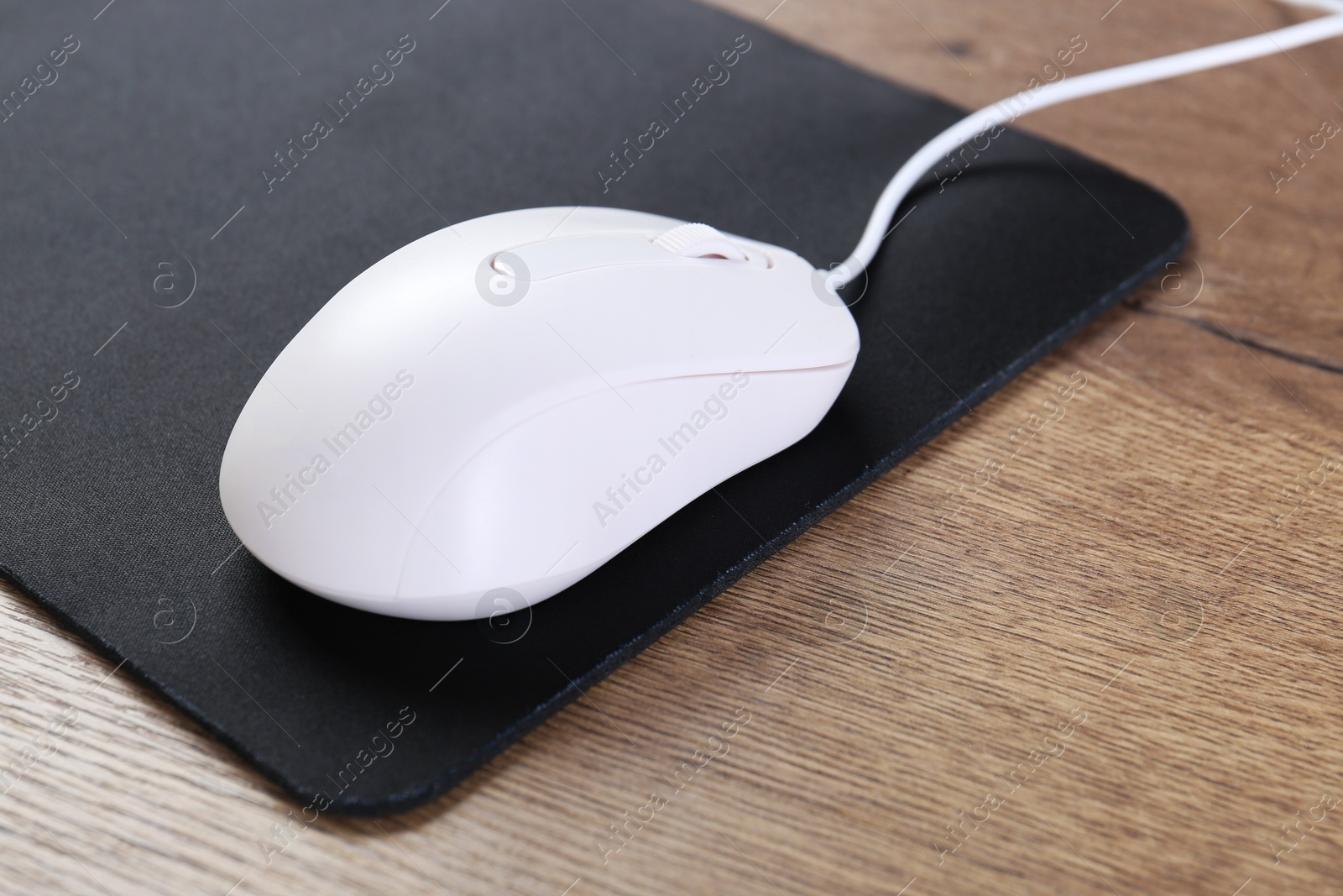 Photo of Computer mouse with mousepad on wooden table, closeup