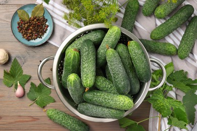 Fresh green cucumbers in colander and spices on wooden table, flat lay