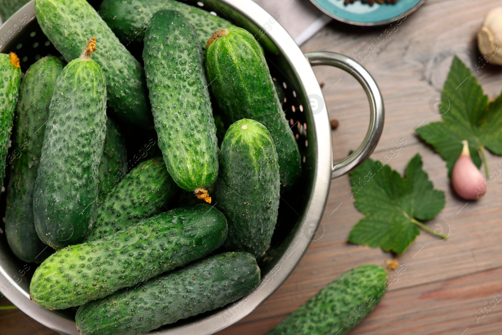 Photo of Fresh green cucumbers in colander on wooden table, top view