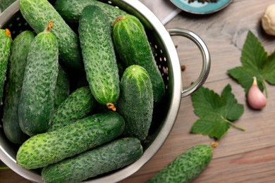 Photo of Fresh green cucumbers in colander on wooden table, top view