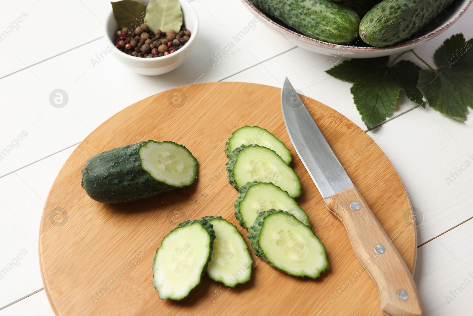 Photo of Fresh cut cucumber, spices and knife on white wooden table