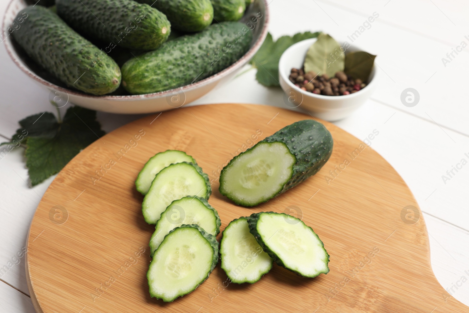 Photo of Fresh whole and cut cucumbers with spices on white wooden table