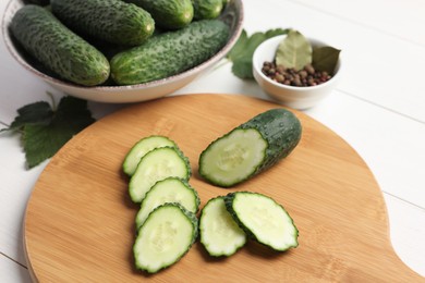 Photo of Fresh whole and cut cucumbers with spices on white wooden table