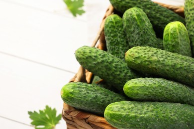 Fresh green cucumbers in wicker box on white table, closeup