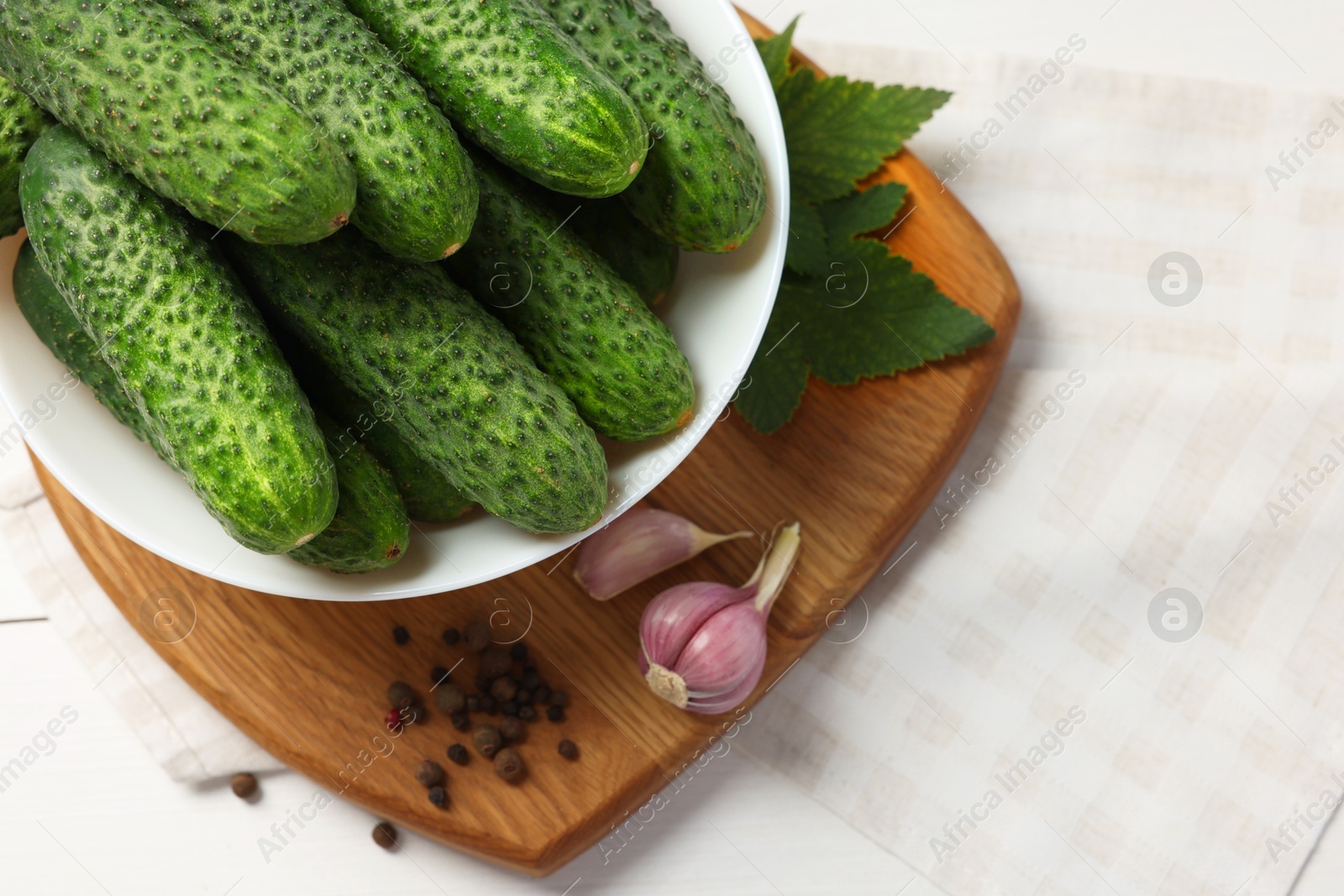 Photo of Fresh green cucumbers in bowl and spices on white table, closeup