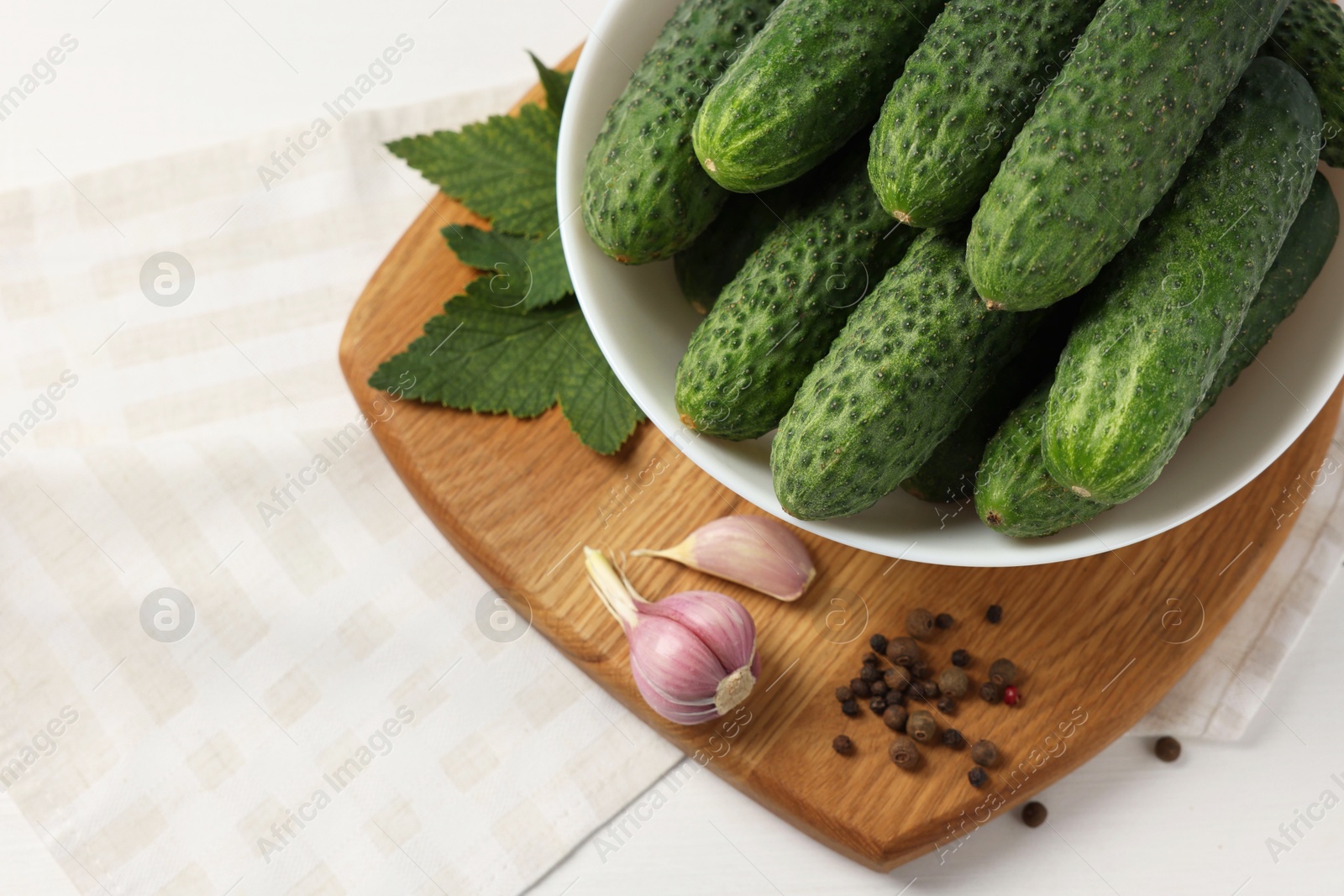 Photo of Fresh green cucumbers in bowl and spices on white table, above view