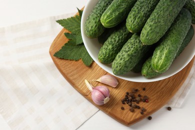 Photo of Fresh green cucumbers in bowl and spices on white table, above view