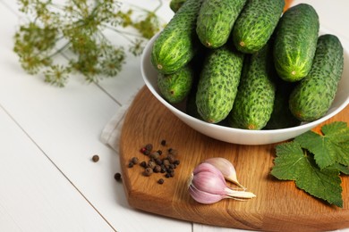 Photo of Fresh green cucumbers in bowl and spices on white wooden table, closeup