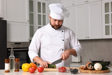 Professional chef cutting cucumber at white marble table in kitchen