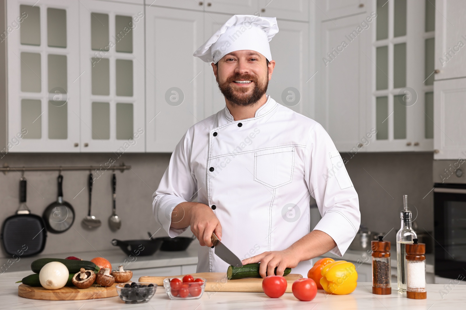 Photo of Professional chef cutting cucumber at white marble table in kitchen