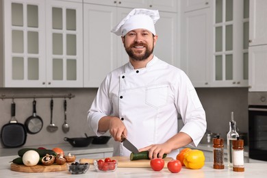 Photo of Professional chef cutting cucumber at white marble table in kitchen