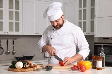 Professional chef cutting tomato at table in kitchen