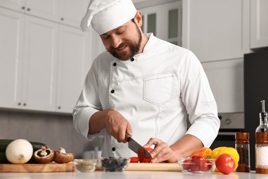 Photo of Professional chef cutting tomato at table in kitchen