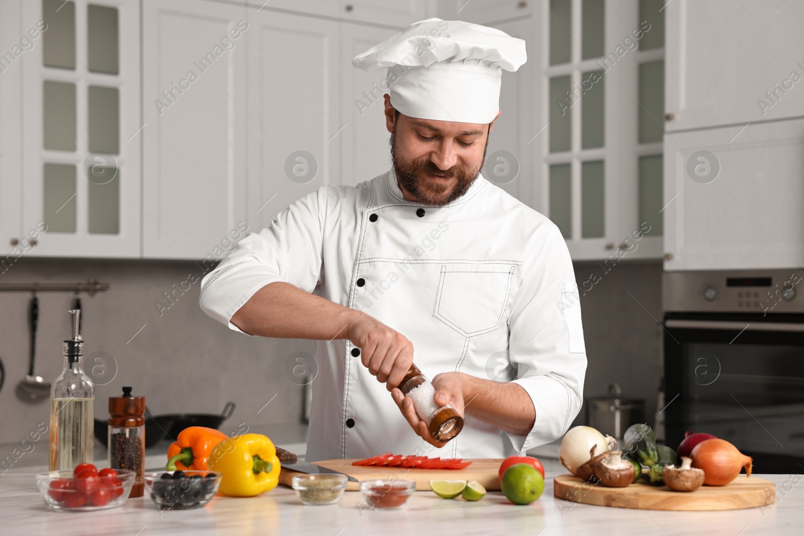 Photo of Professional chef adding salt to tomato at table in kitchen, closeup