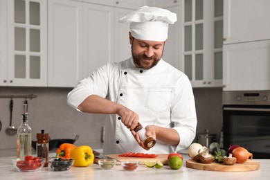 Professional chef adding salt to tomato at table in kitchen, closeup