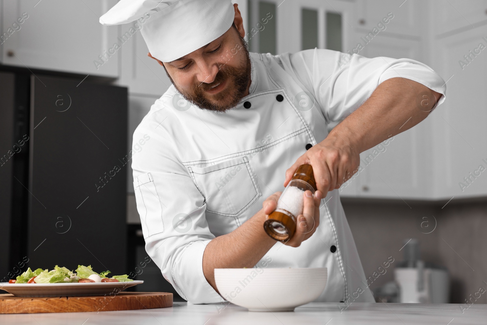 Photo of Professional chef adding salt into bowl at table in kitchen