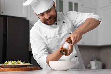 Professional chef adding salt into bowl at table in kitchen