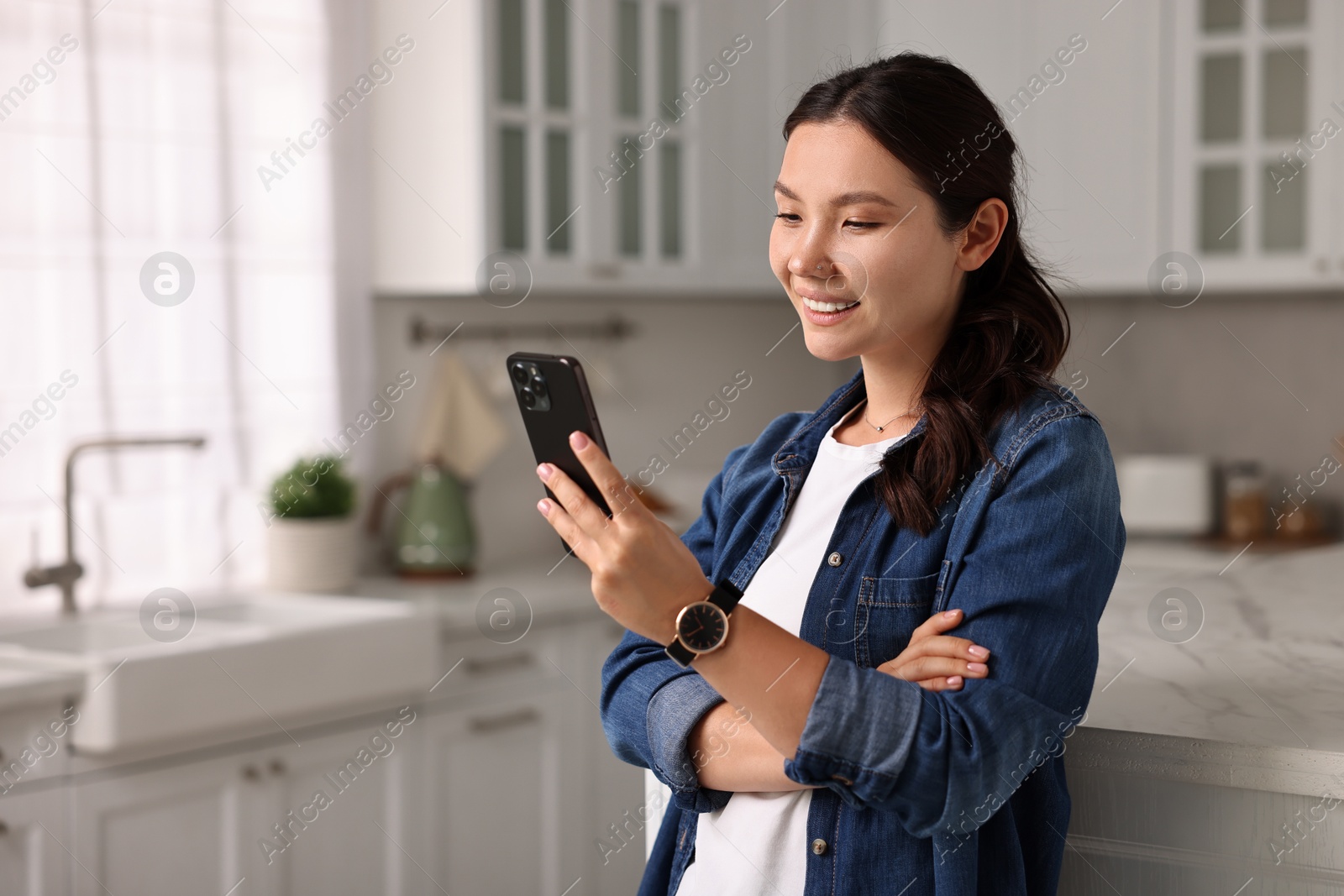 Photo of Smiling woman using smartphone in kitchen. Space for text