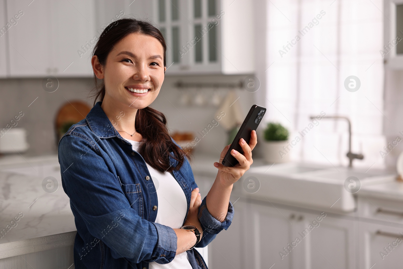 Photo of Smiling woman with smartphone in kitchen. Space for text