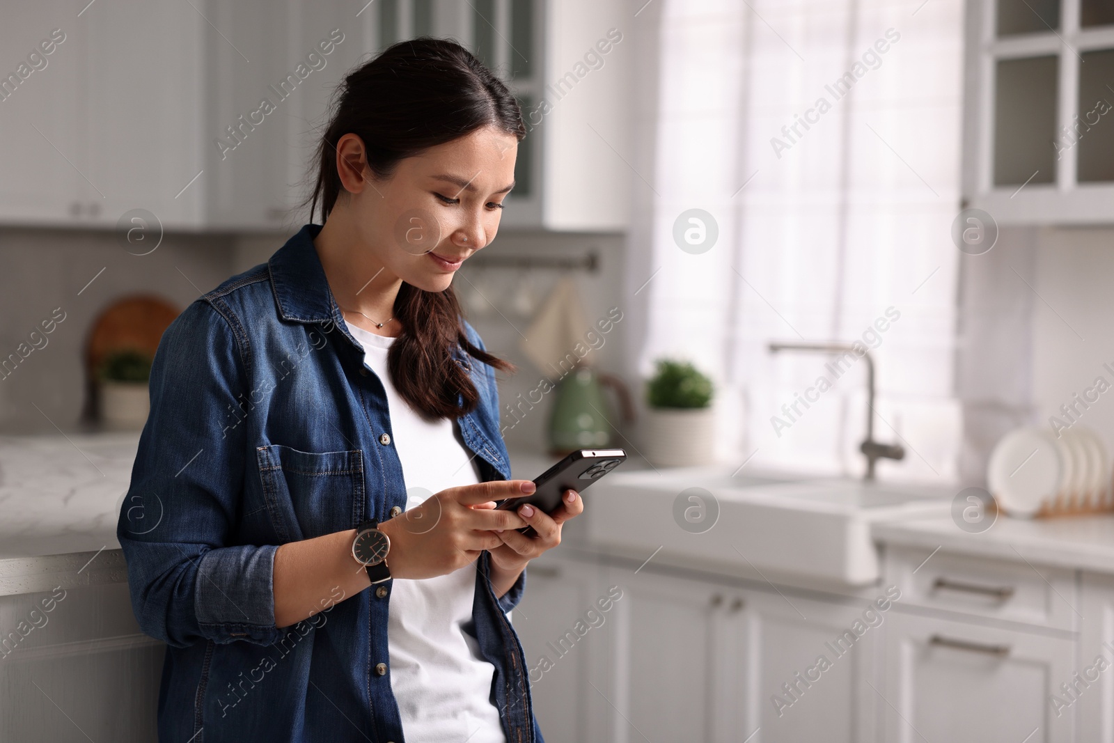 Photo of Beautiful woman using smartphone in kitchen. Space for text