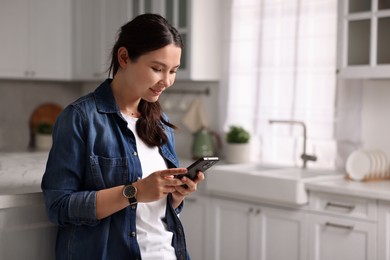 Beautiful woman using smartphone in kitchen. Space for text