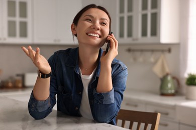 Smiling woman talking on smartphone at table in kitchen