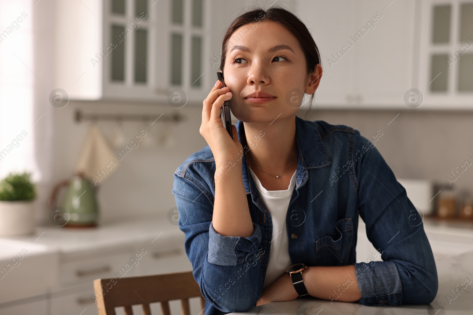 Photo of Beautiful woman talking on smartphone in kitchen