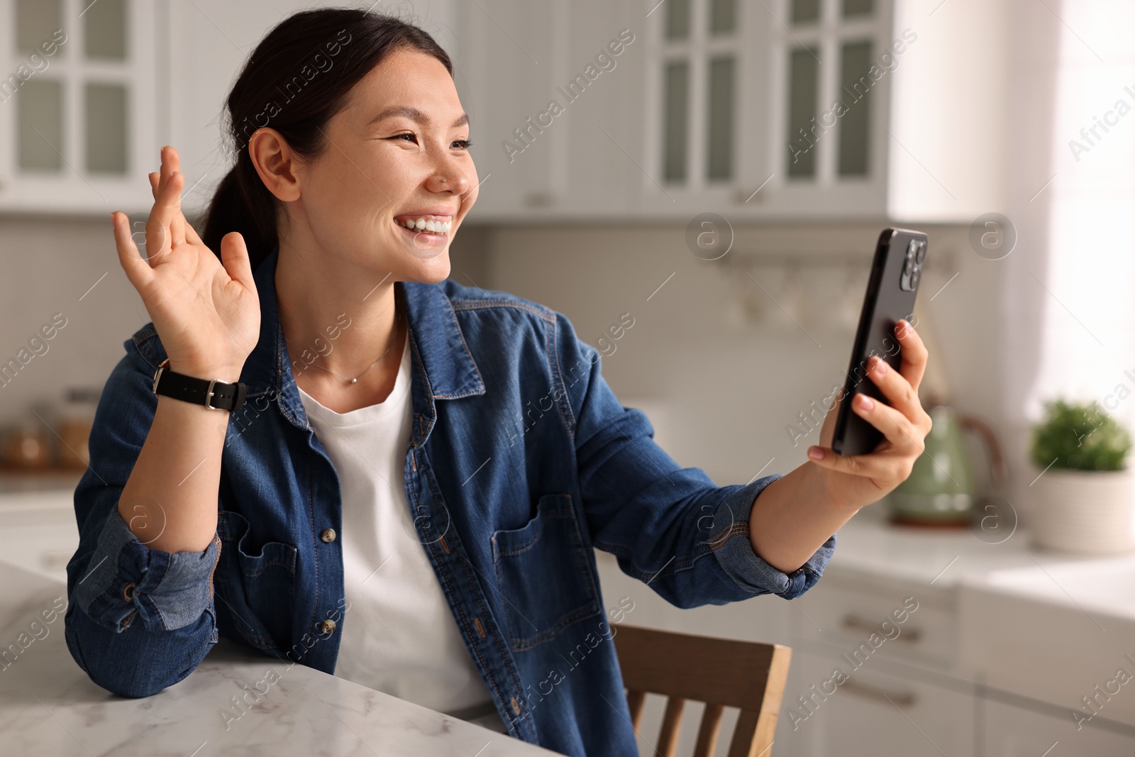 Photo of Smiling woman having video chat by smartphone in kitchen