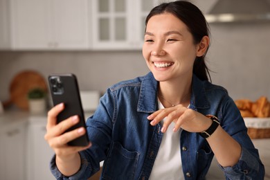 Smiling woman having video chat by smartphone in kitchen