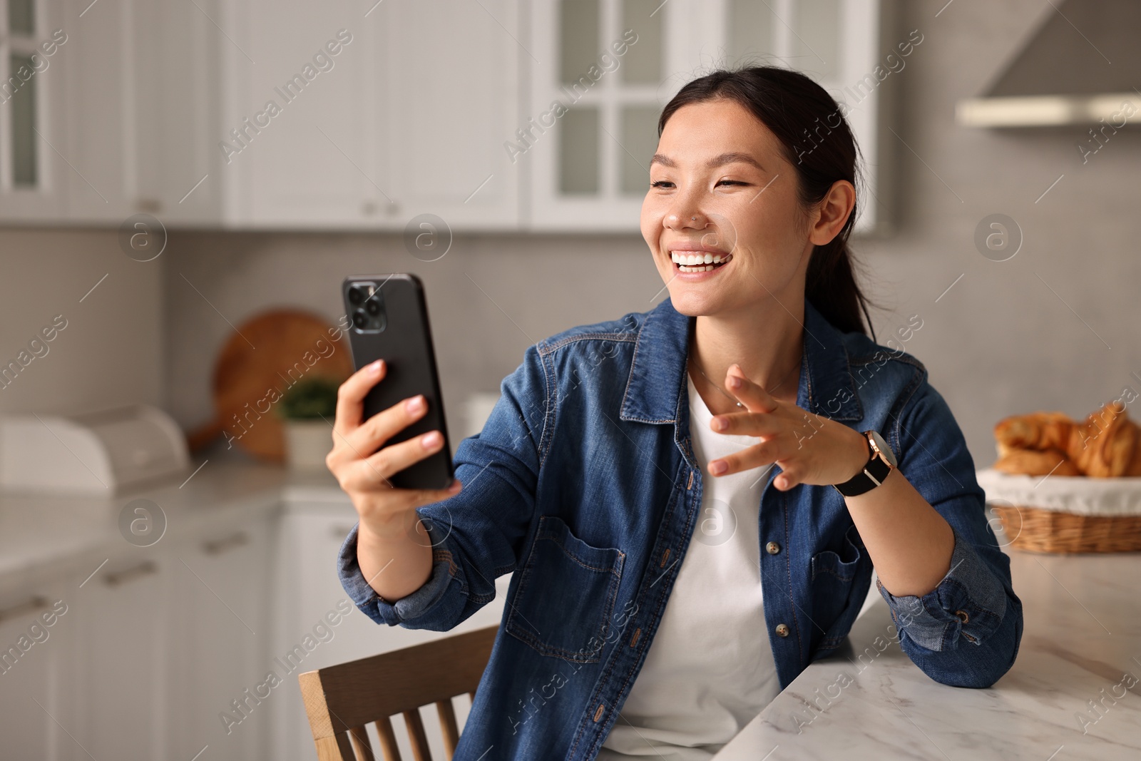 Photo of Smiling woman having video chat by smartphone in kitchen