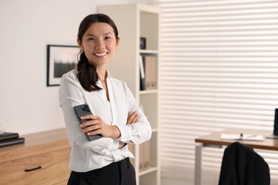 Smiling businesswoman with smartphone in office. Space for text