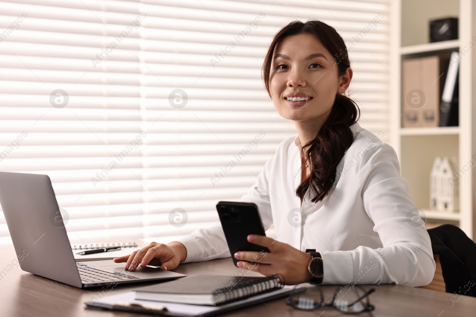 Photo of Smiling businesswoman with smartphone at table in office