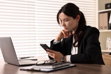 Photo of Beautiful young businesswoman using smartphone in office