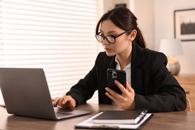 Photo of Beautiful businesswoman with smartphone at table in office