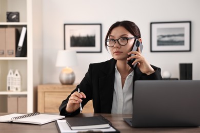 Photo of Beautiful businesswoman talking on smartphone at table in office